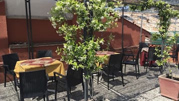 Una veranda esterna con tavoli e sedie, un pergolato e piante in vaso.