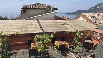 A rooftop terrace with outdoor seating, a view of the sea, and terracotta-tiled buildings.