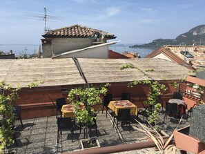 A rooftop terrace with outdoor seating, a view of the sea, and terracotta-tiled buildings. - Hotel Cortina (Garda)
