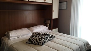 A hotel room with a bed, a zebra-patterned pillow, and a wooden wardrobe. - Hotel Cortina (Garda)