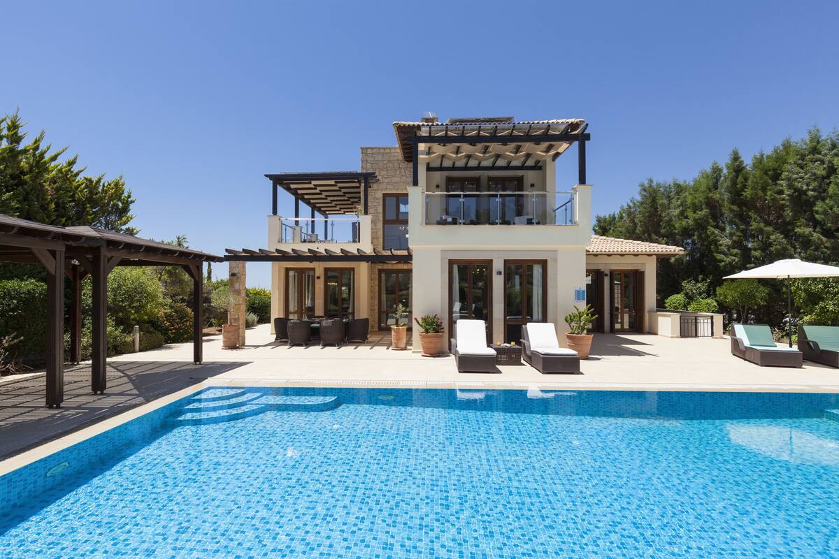 A two-story house with a swimming pool, outdoor seating, and a pergola.
