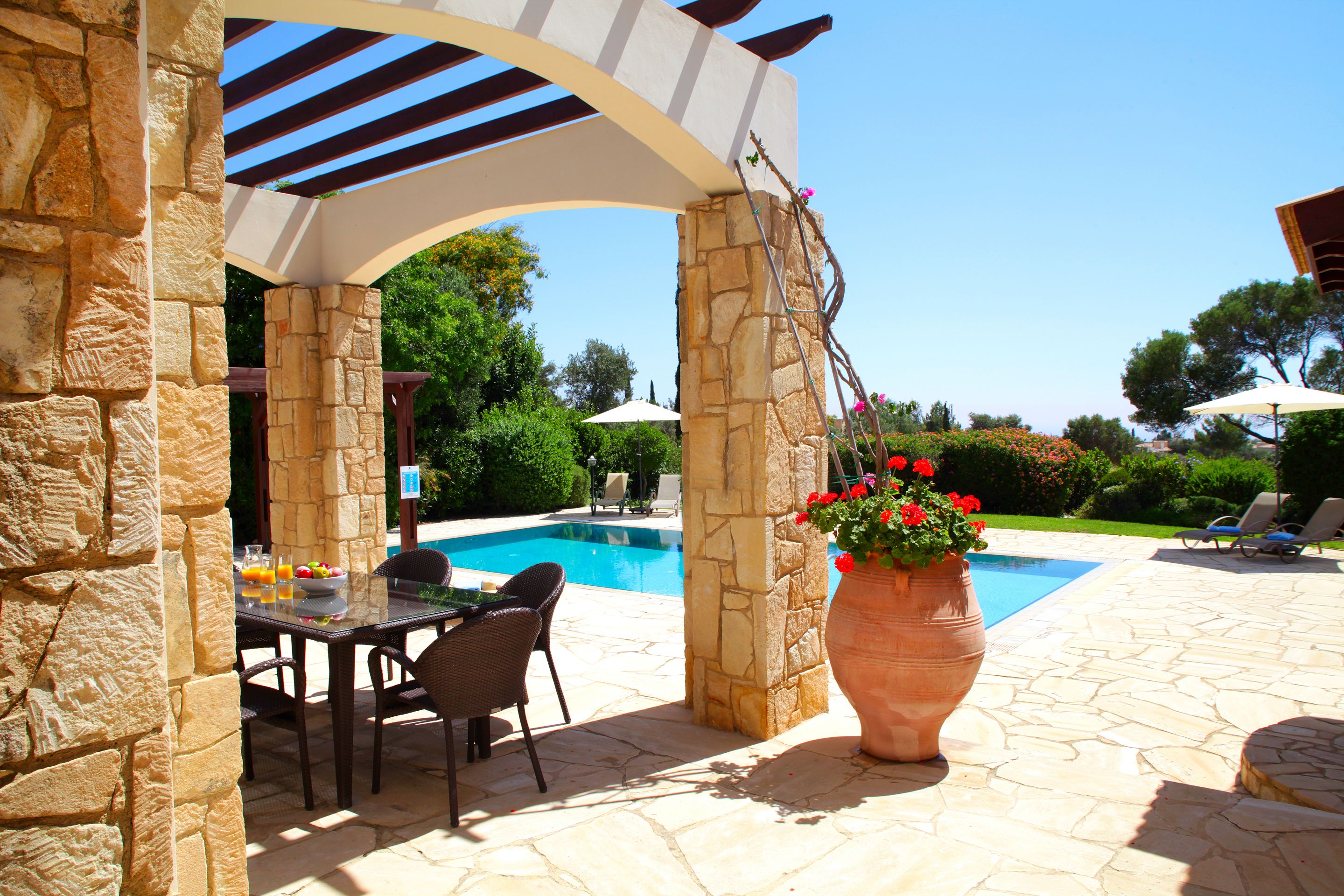 An outdoor pool area with stone pillars, a table with chairs, and a large flower pot.