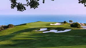 A golf course with sand bunkers and a flag on a green, overlooking a body of water. - Aphrodite Hills Rentals – Superior Villas (Kouklia)