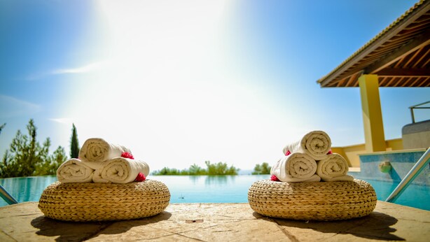 Two woven baskets with rolled towels and pink flowers by a poolside. - Aphrodite Hills Rentals – Superior Villas (Kouklia)