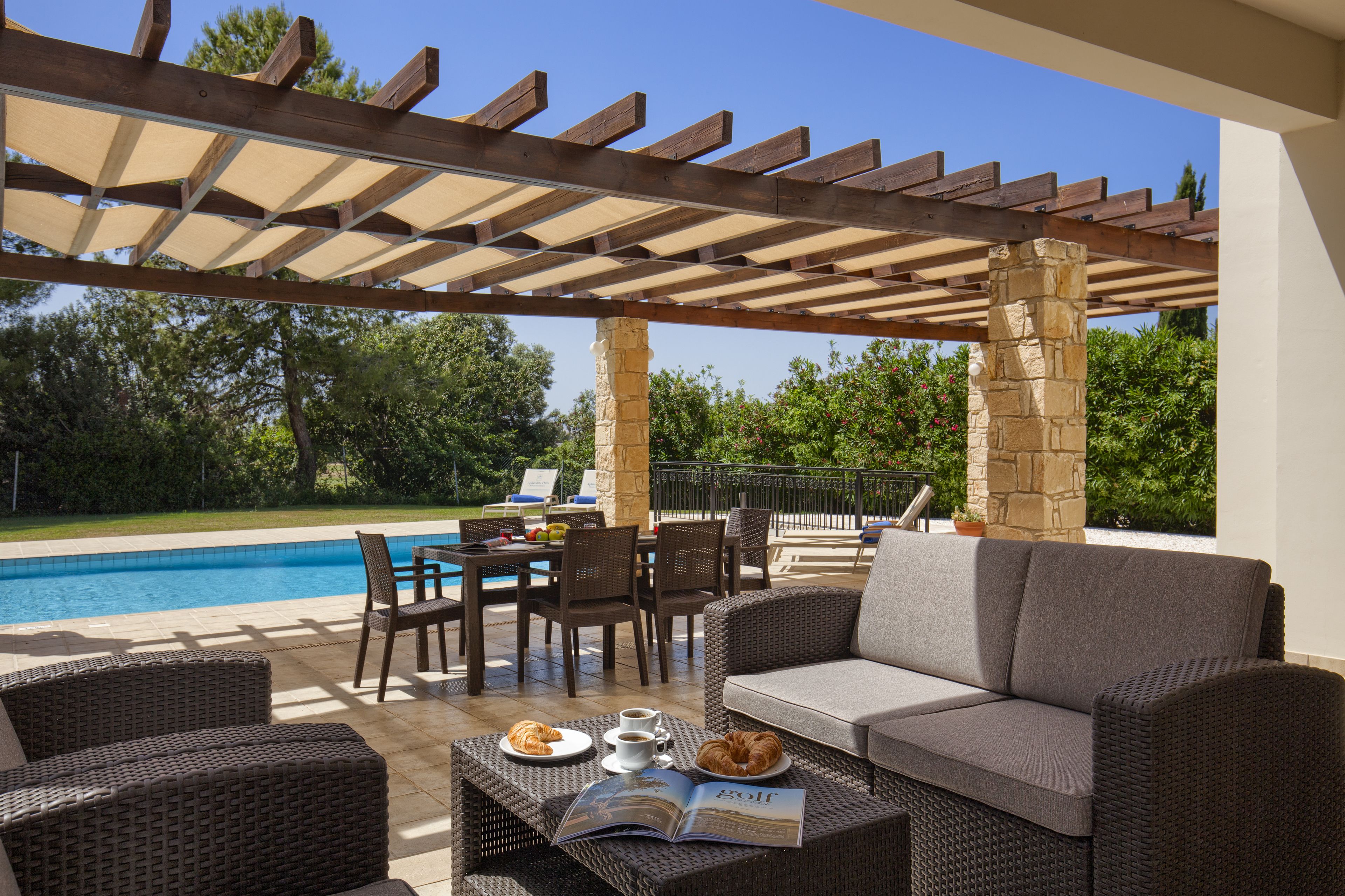 Un'area patio esterna con mobili in vimini, una piscina e un pergolato.