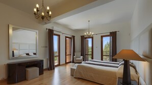 A spacious bedroom with a large bed, a desk, a chair, and a chandelier. - Aphrodite Hills Rentals – Superior Villas (Kouklia)