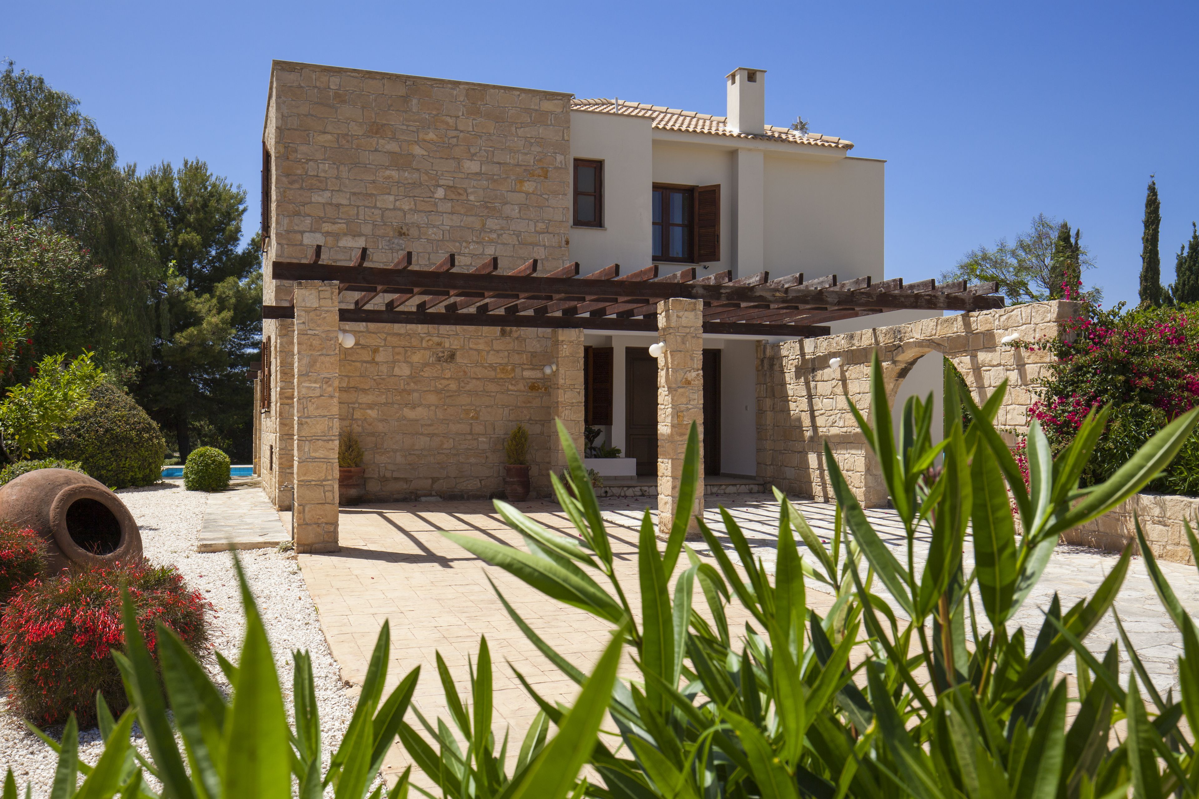 Una casa moderna con fachada de piedra, un porche cubierto y un jardín con diversas plantas y flores.