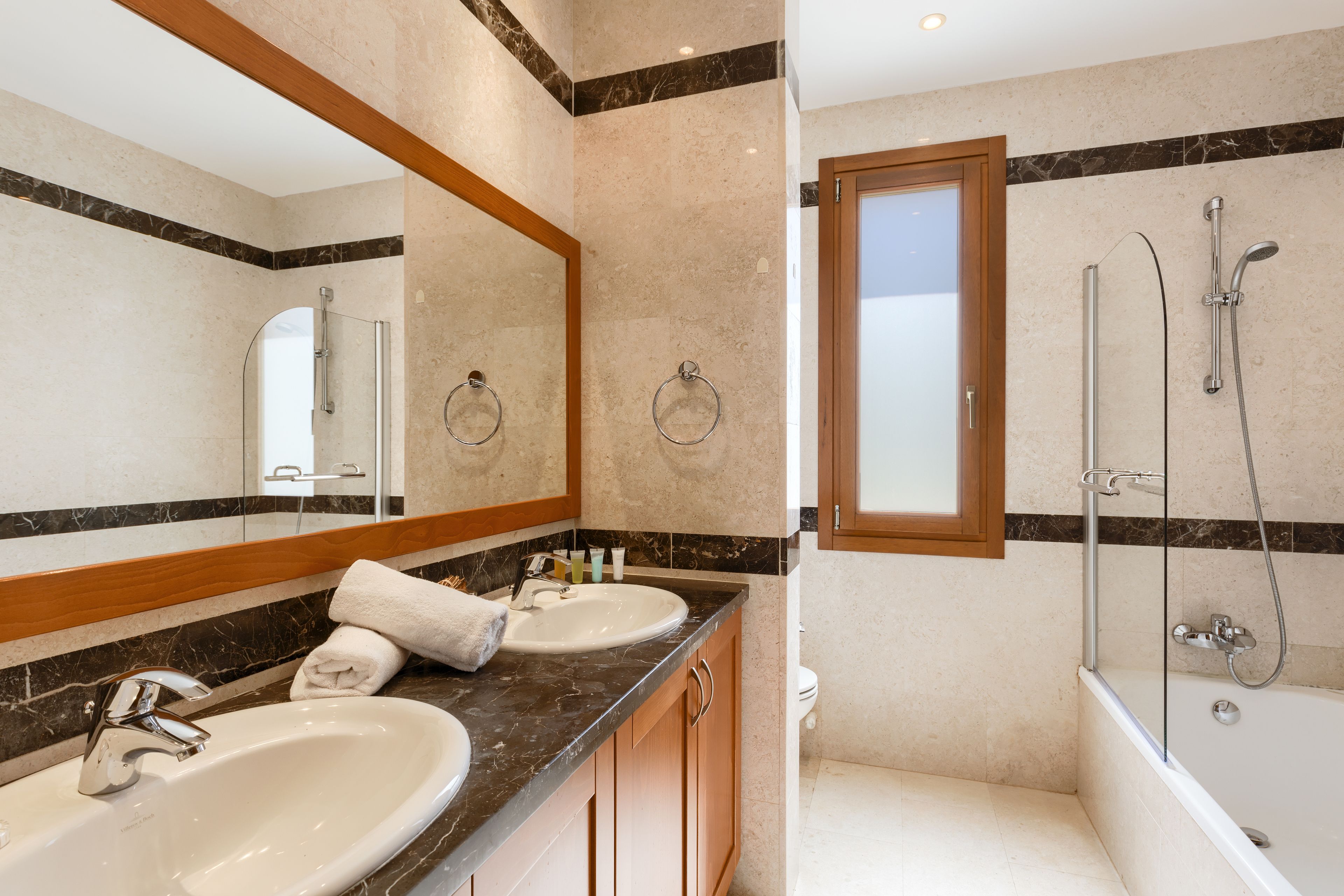 A modern bathroom with two sinks, a large mirror, and a walk-in shower.