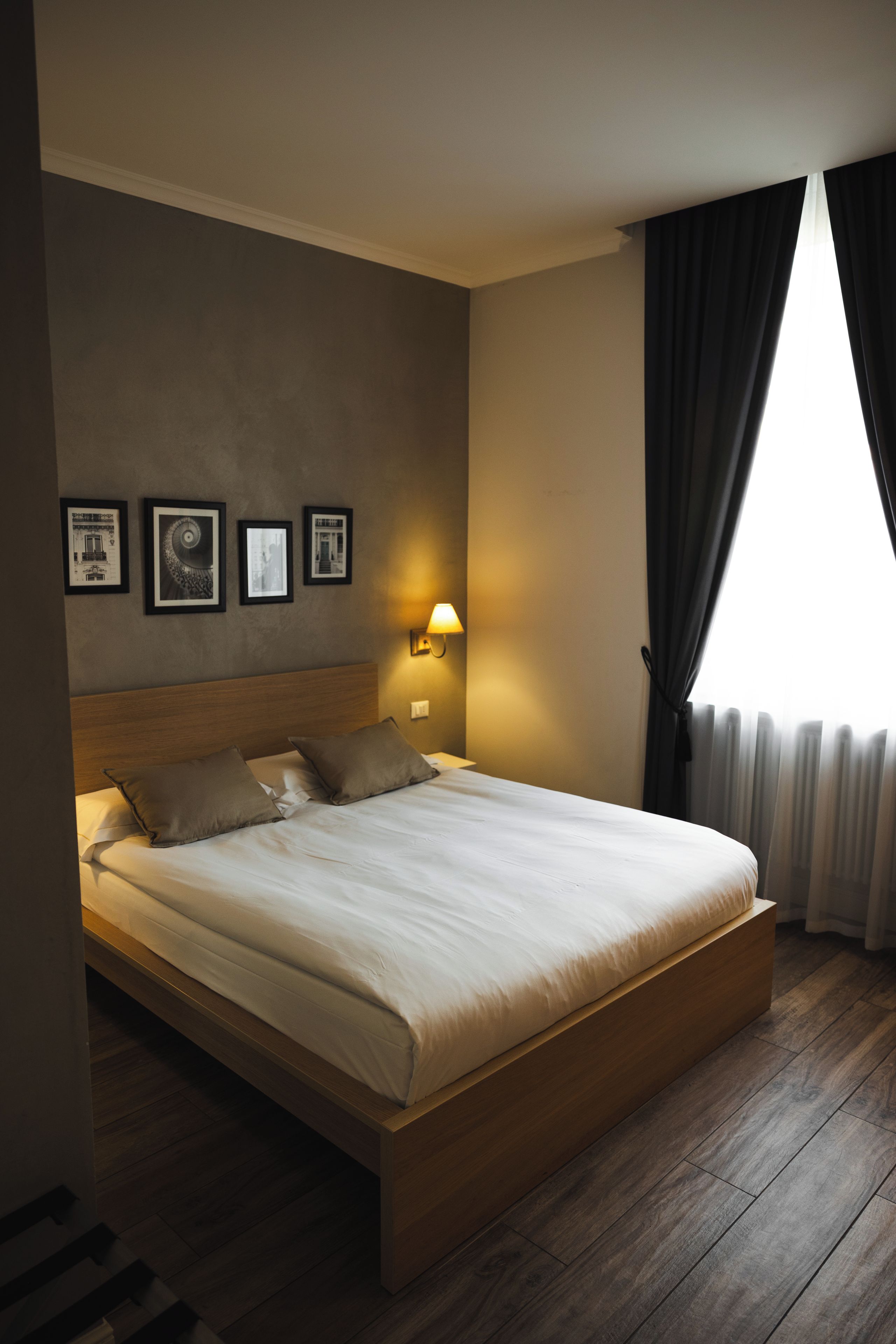 Una habitación de hotel moderna con una cama grande, un cabecero, una lámpara de noche y cuadros enmarcados en la pared.