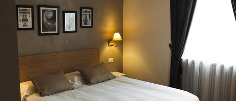 Una habitación de hotel moderna con una cama grande, un cabecero, una lámpara de noche y cuadros enmarcados en la pared.