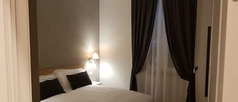A hotel room with a bed, a nightstand, a lamp, and sheer curtains.