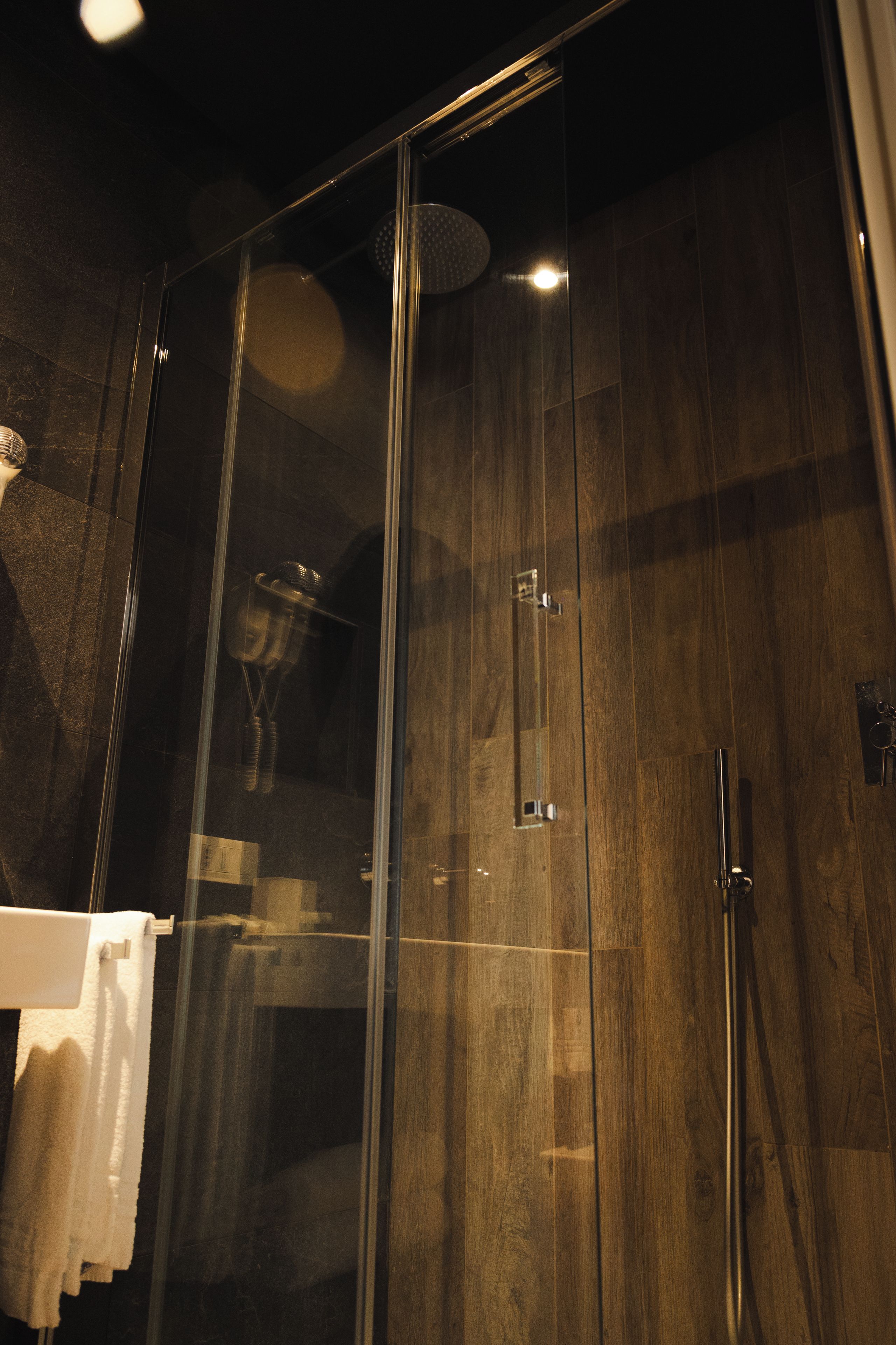 A glass-enclosed shower with a wooden panel wall, a towel rack, and a visible shower head.