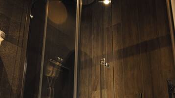 A glass-enclosed shower with a wooden panel wall, a towel rack, and a visible shower head.