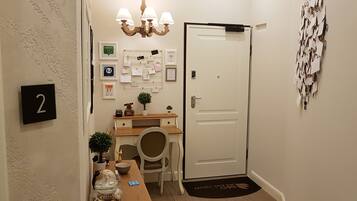 Un pasillo con un escritorio, una silla y una puerta con cerradura. En la pared hay cuadros enmarcados y un tablón de anuncios.