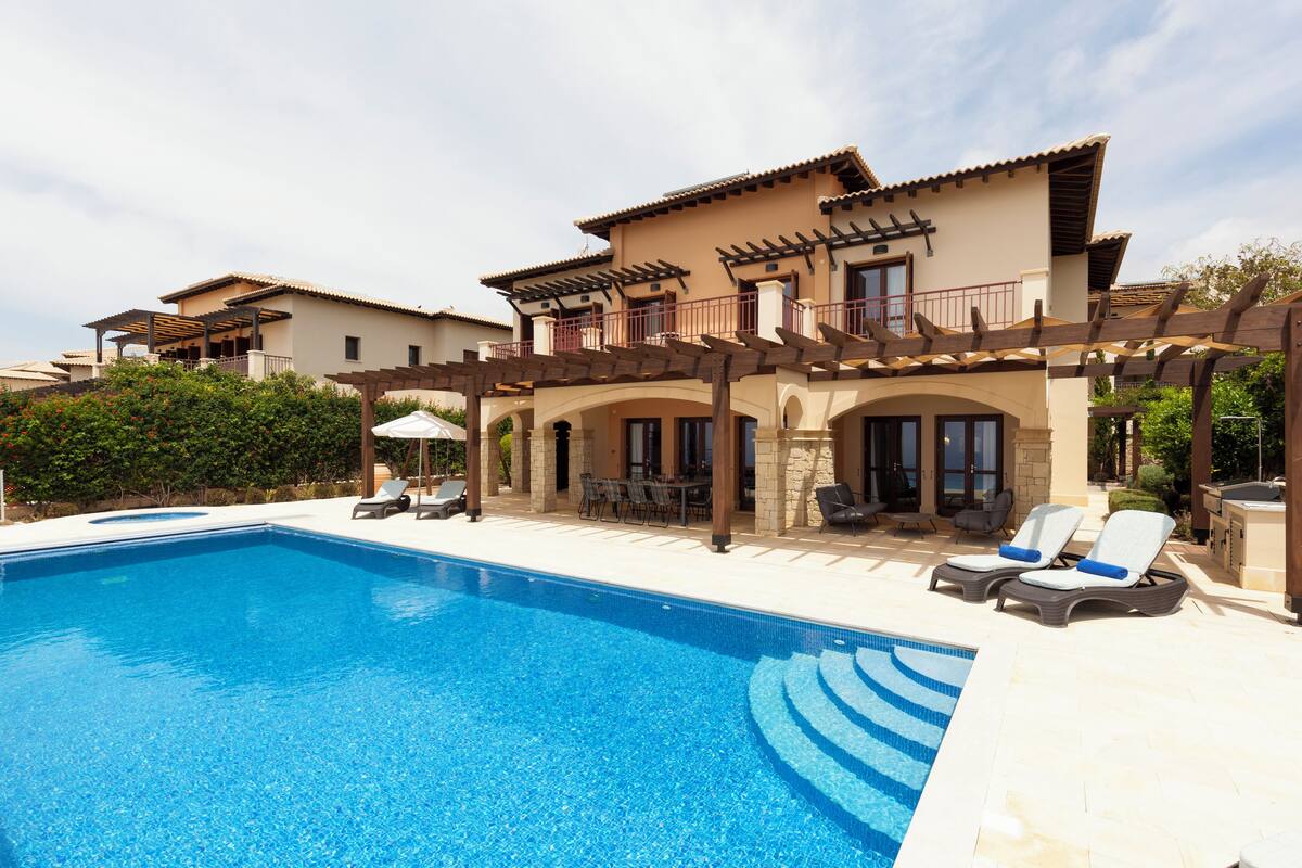 Una piscina con sillones de descanso y un patio techado.