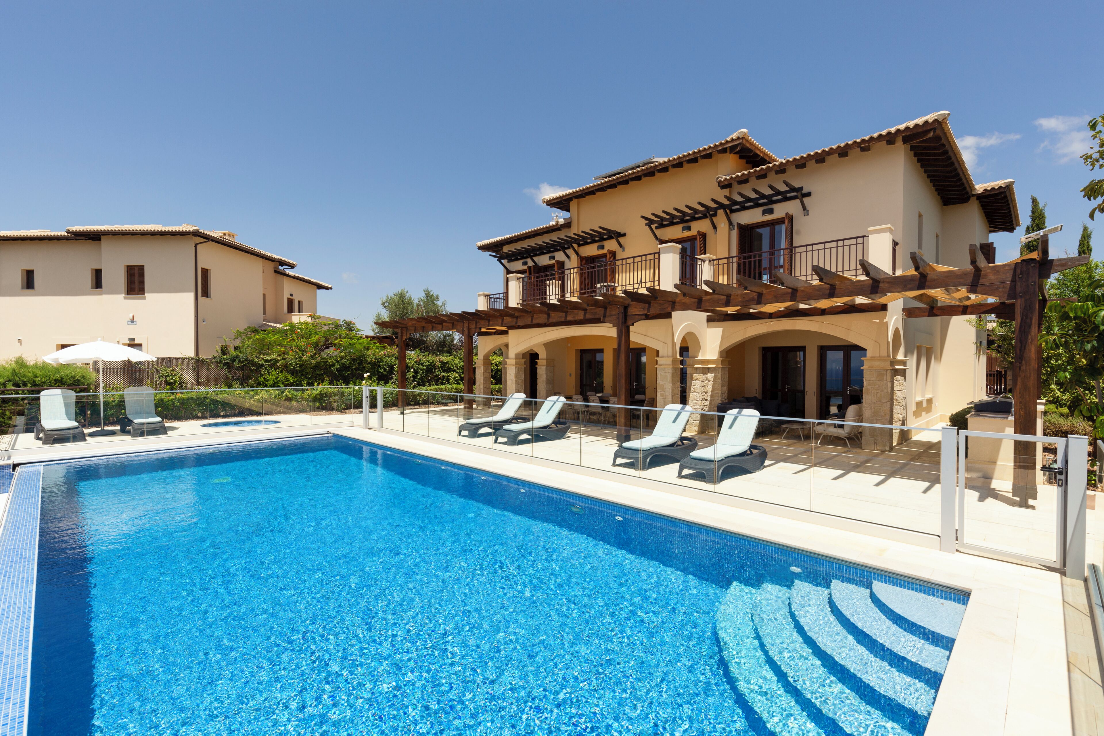 A swimming pool with lounge chairs, a pergola, and a building with balconies.