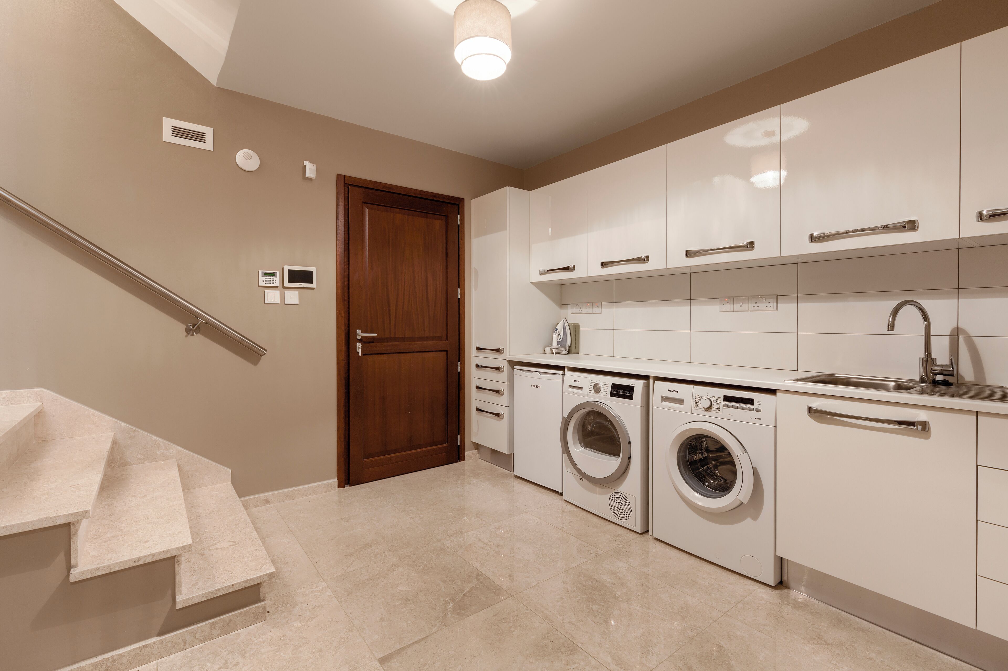 A modern kitchen with a built-in washer and dryer, a stainless steel sink, and a wooden door.