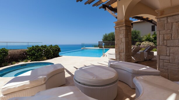 Zona junto a la piscina con vista al océano, mobiliario exterior y una estructura de pérgola.