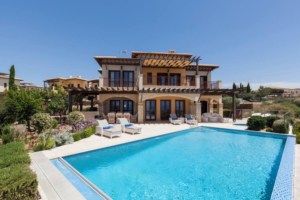 Una casa de dos pisos con piscina, mobiliario de exterior y jardín.