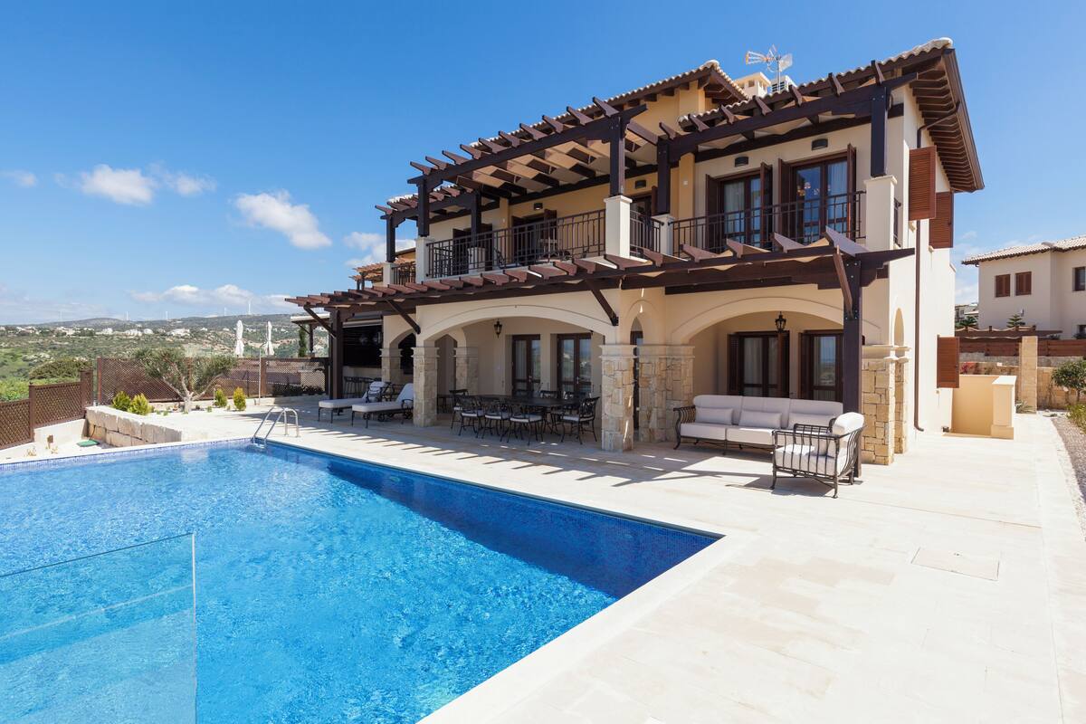 Una casa de dos pisos con piscina, mobiliario exterior y vista al paisaje.