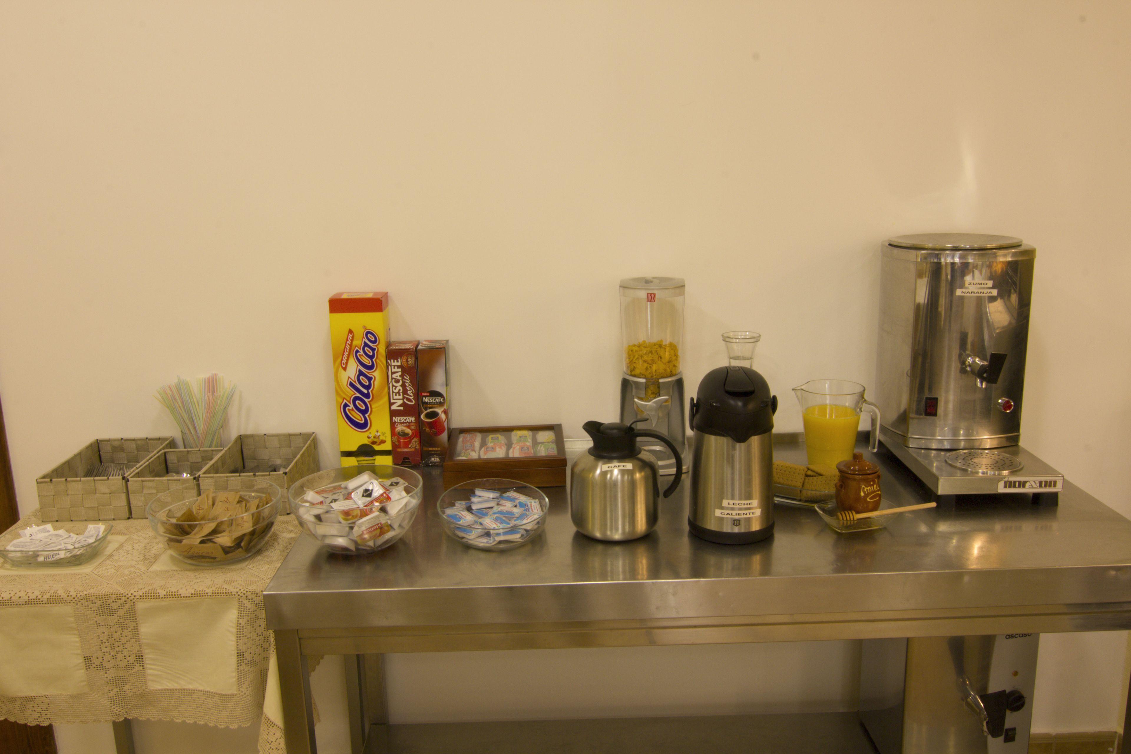 Een roestvrijstalen tafel met verschillende keukenbenodigdheden, waaronder een koffiezetapparaat, een blender en bakjes met eten.