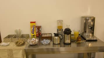 Een roestvrijstalen tafel met verschillende keukenbenodigdheden, waaronder een koffiezetapparaat, een blender en bakjes met eten.