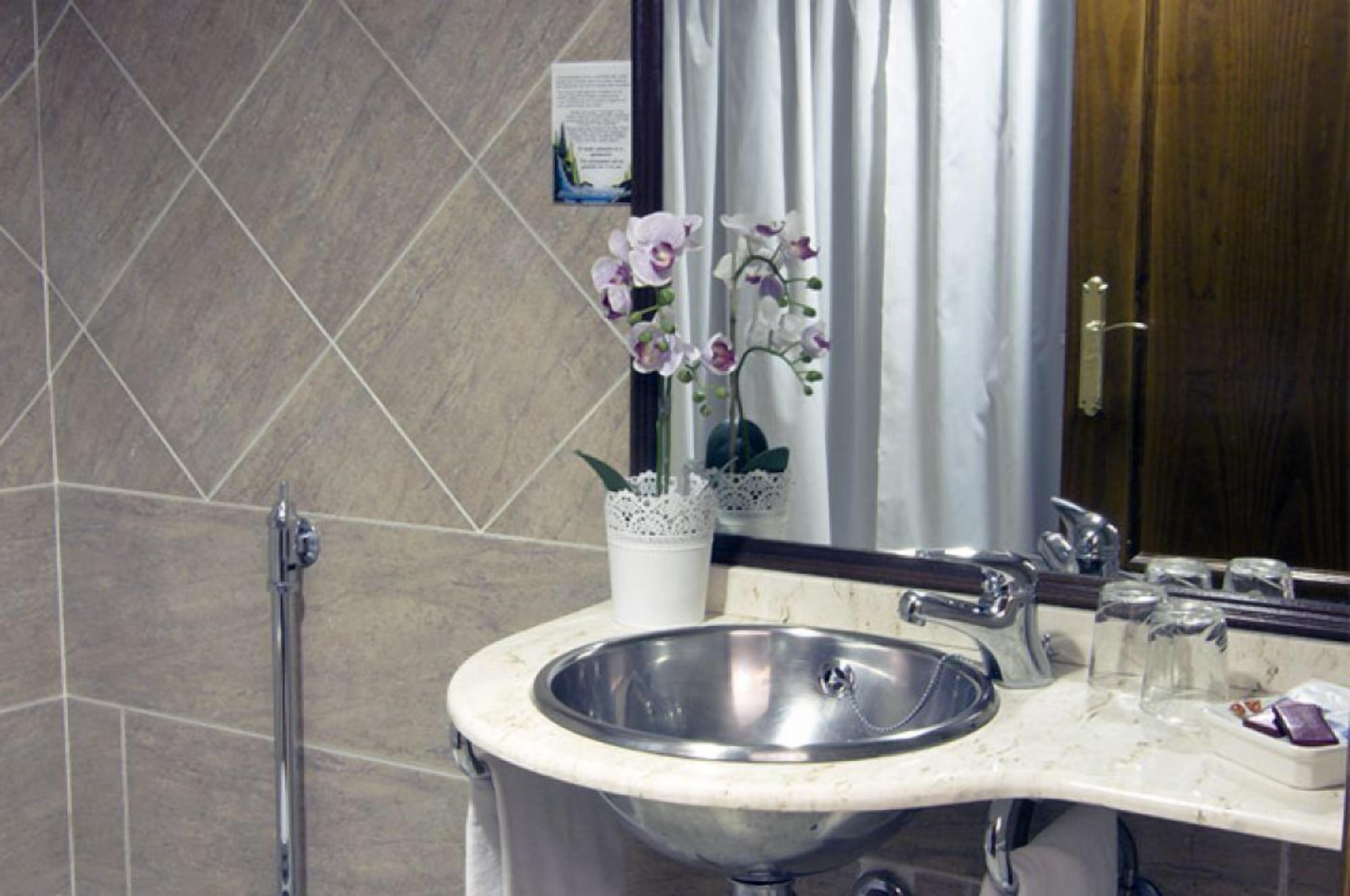 A bathroom with a marble sink, a hand dryer, and a potted orchid.