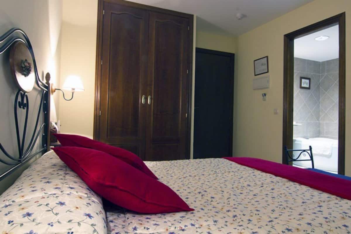 Quarto com cama, guarda-roupa de madeira, espelho e janela com vista para um banheiro.