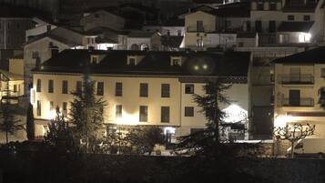 Vista nocturna de un pueblo con edificios iluminados por farolas, un muro de piedra y una valla en primer plano.