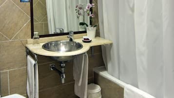 Un baño con lavamanos, espejo y una orquídea en maceta.
