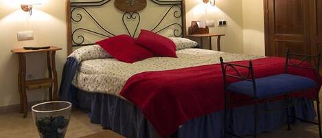 A neatly arranged bedroom with a bed, bedside tables, a nightstand, a chair, and a vase with flowers.