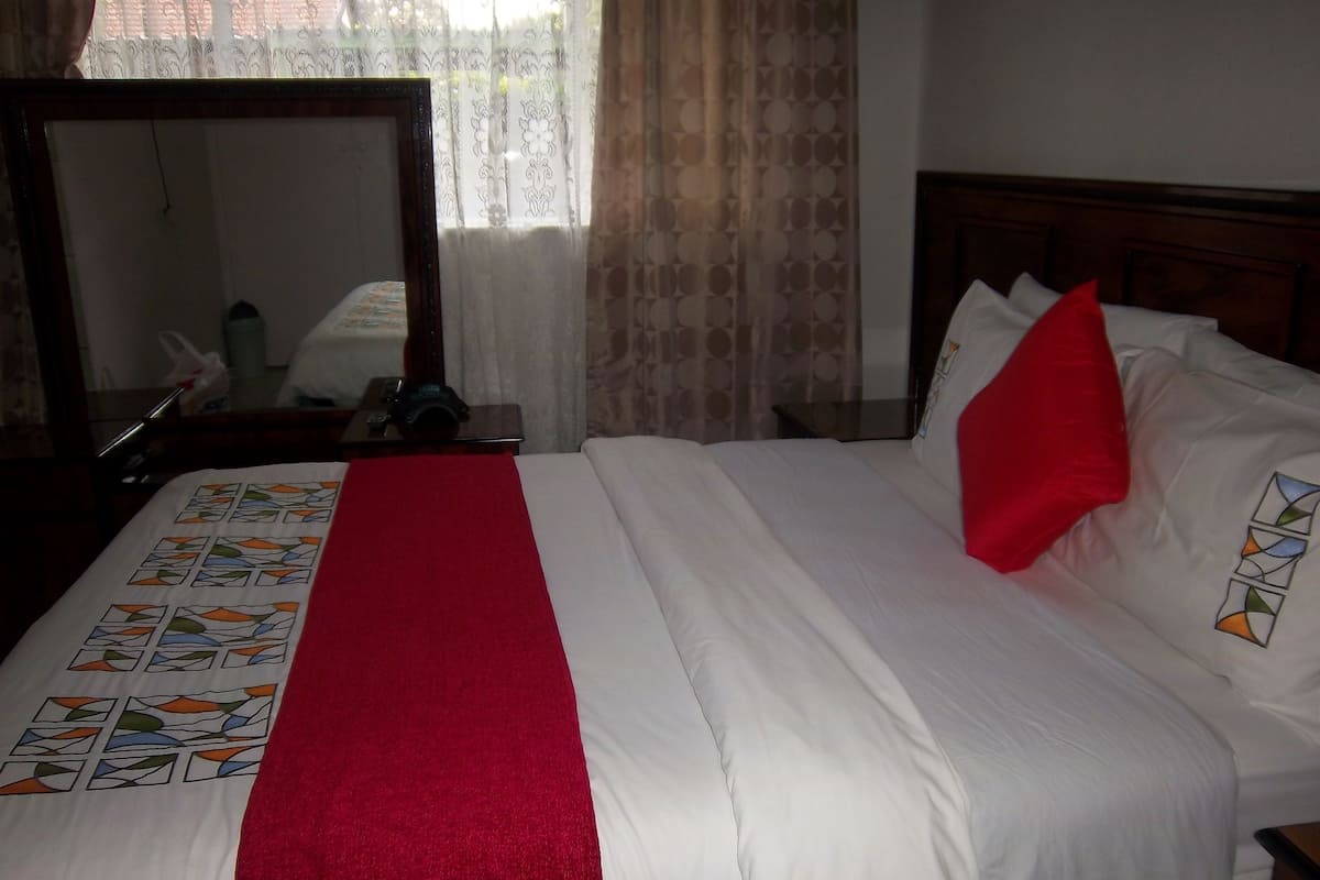 A hotel room with a neatly made bed, a red throw blanket, and a mirror on the wall.