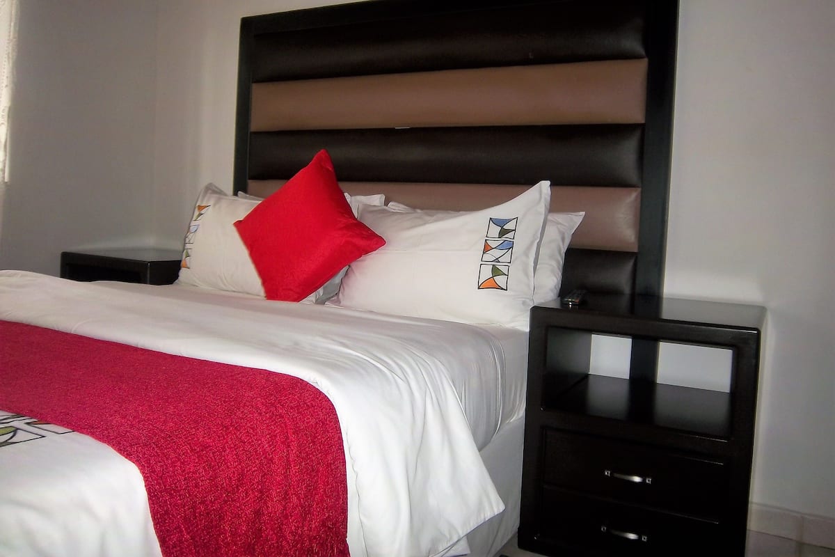 A neatly made bed with a red throw blanket and a white comforter, a black headboard, and two bedside tables with black frames.