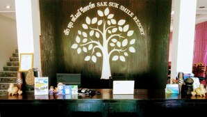 A reception desk with a tree mural, a computer, and a small seating area. - SakSukSmile Resort (Sukhothai)