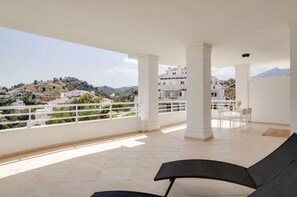 A balcony with a view of a hilly landscape, white pillars, and a table with chairs.