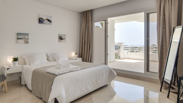 A modern hotel room with a large bed, a desk, and a balcony with a city view.