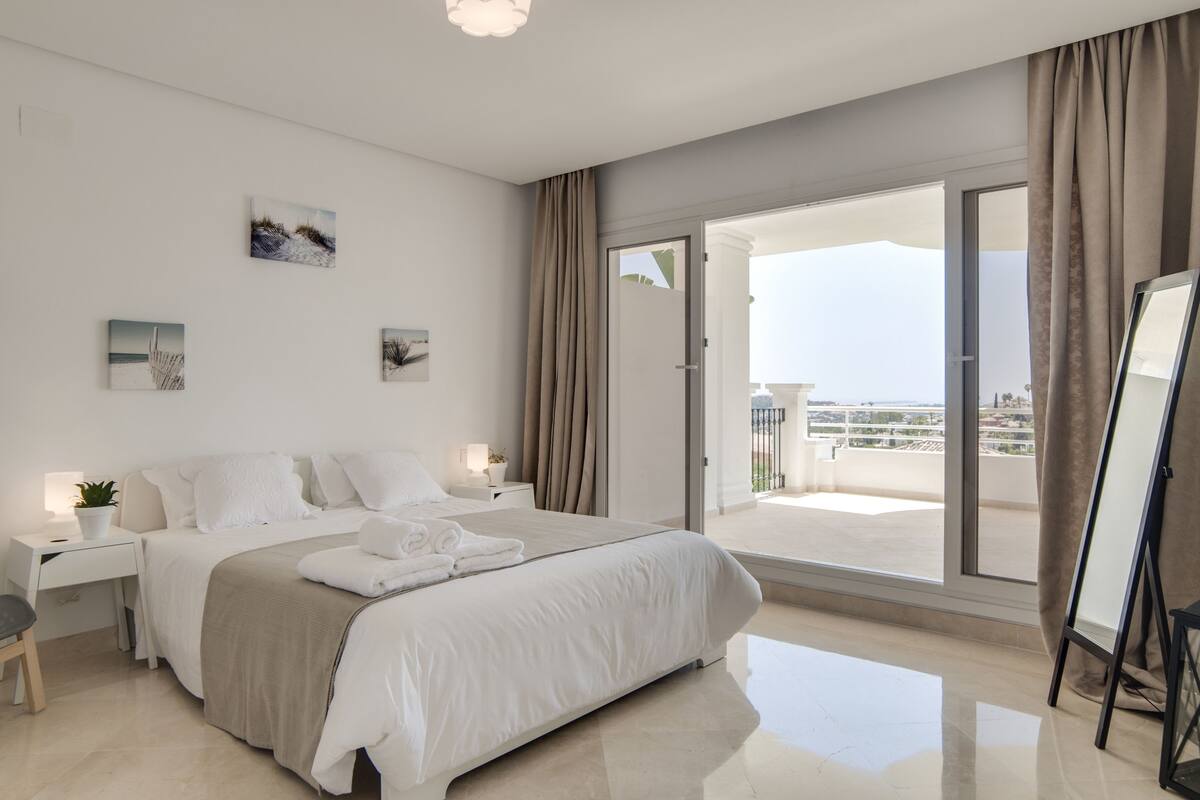 Una habitación de hotel moderna con una cama grande, un escritorio y un balcón con vistas a la ciudad.