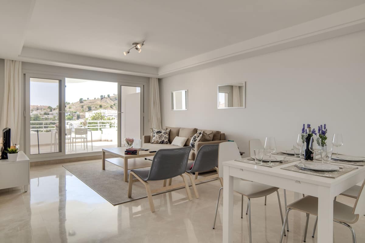 Amplia sala de estar con sofá, mesa de comedor y sillas. Balcón con vistas al paisaje.