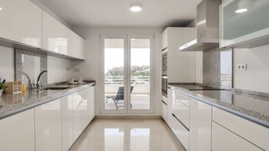 A modern kitchen with white cabinets, granite countertops, and a view of the city through large sliding doors.