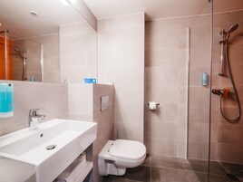 Un baño moderno con un lavabo blanco, un inodoro y una zona de ducha con mampara de vidrio.