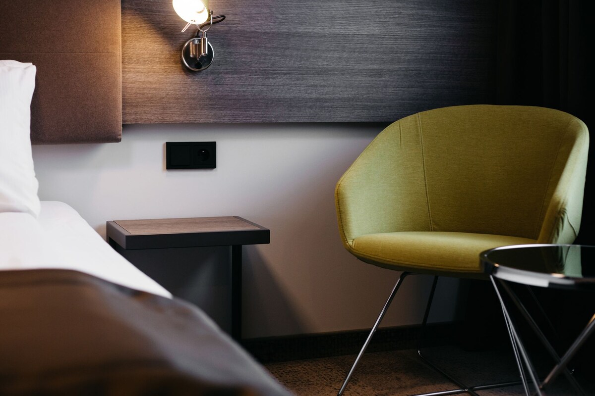 A hotel room with a bed, a nightstand, a lamp, and a yellow armchair.