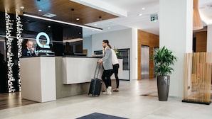 A hotel reception area with a modern design, including a reception desk, a large potted plant, and a blue carpet with the hotel logo. - Q Hotel Plus Katowice (Katowice)