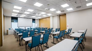 A conference room with rows of tables and chairs, a projector screen, and a whiteboard.