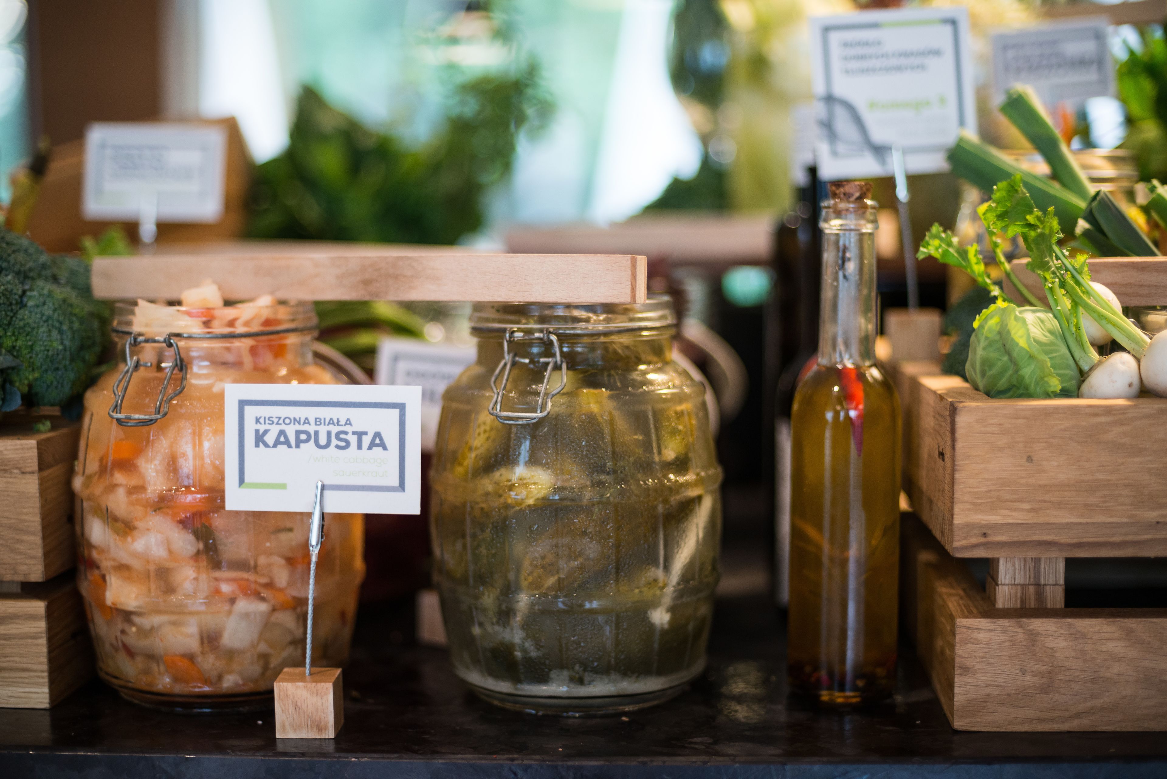 A display of preserved foods including jars of pickled vegetables and a bottle of oil, with wooden crates and labels.