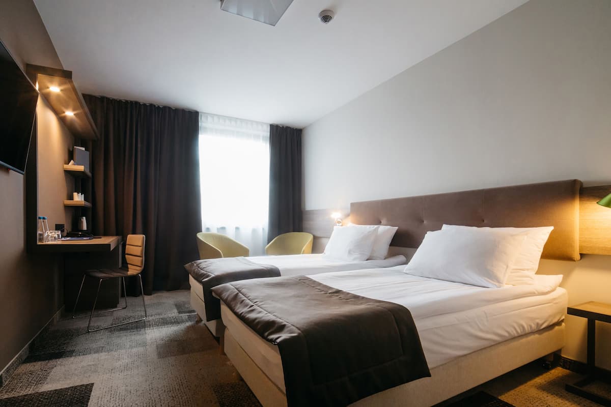 Ein Hotelzimmer mit einem großen Bett, zwei Nachttischen, einem Schreibtisch mit Stuhl und einem Fernseher.