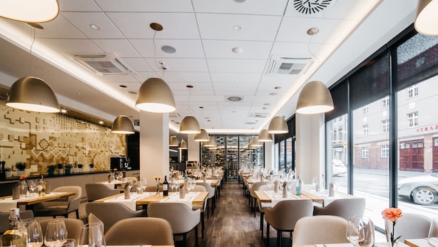 A restaurant interior with long tables, chairs, pendant lighting, and a view of the street outside. - Q Hotel Plus Katowice (Katowice)