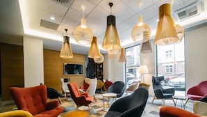 A modern lounge area with multiple seating options, including armchairs and sofas, and a large window providing a view of the street. - Q Hotel Plus Katowice (Katowice)