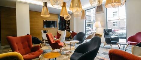 A modern lounge area with multiple seating options, including armchairs and sofas, and a large window providing a view of the street.