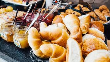 Une table de buffet proposant une variété de pains et de viennoiseries, notamment des croissants et des petits pains, ainsi que des pots de confiture.