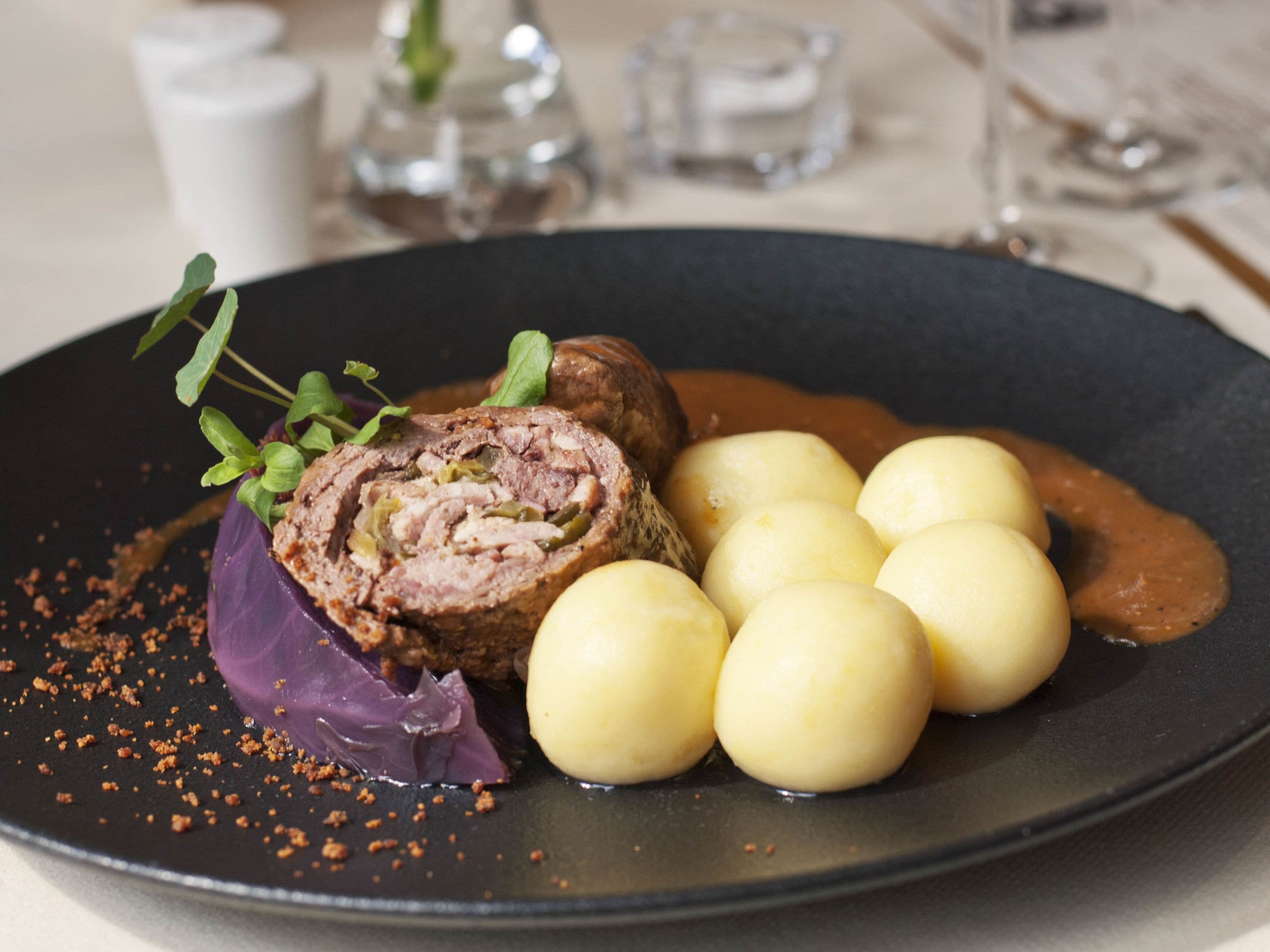 Un plato con un guiso de carne enrollada, patatas hervidas y salsa.